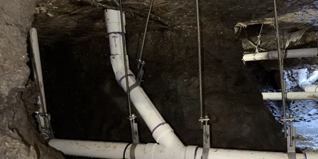 New PVC drain line hung on stainless steel hangers in a crawlspace tunnel