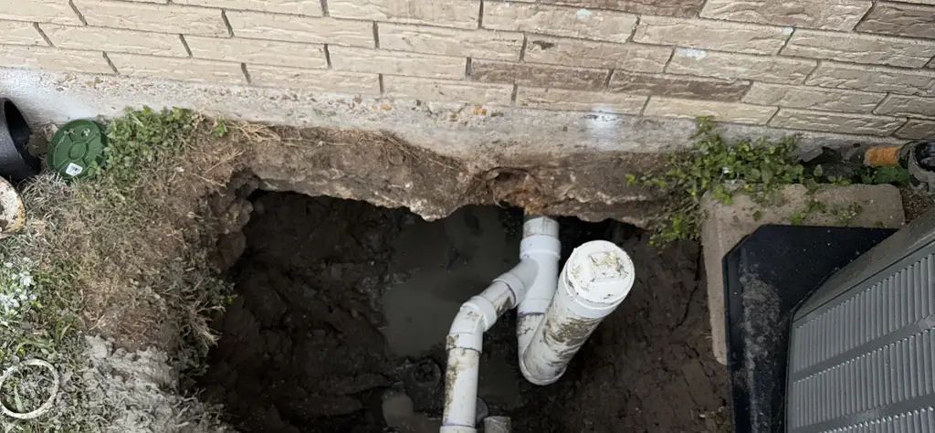 Exterior dig at a brick house foundation with new PVC pipe and a cleanout